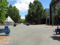 A pedestrian street with trees, benches and a fountain but few people.