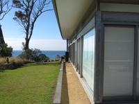 View along the side of a modern glass and steel house by the sea.