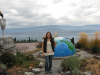 Tammie standing in front of a large globe, half-sunk into the ground. Behind her is a lake and mountains.