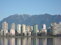 Across an expanse of water stand a crowd of tall apartment blocks, in the background mountains tower over them.