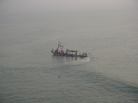 A fishing boat executing a sharp turn, the crew standing on the benches.  The boat is decorated with colourful flags.