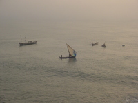 Small fishing canoes in the sea.  One, in the centre of the picture, has a patchwork sail.