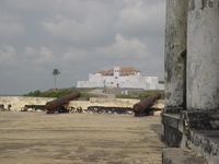 Cannons point over battlements toward a whitewashed castle on a hill