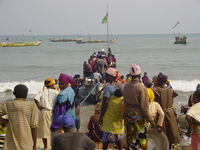 In the foreground women wait with large metal basins.  In the background young boys help to bring in a fishing boat.