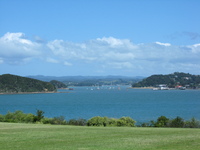 Beyond a lawn lies wind-rippled blue water, dotted with small islands.  There are hills in the background.