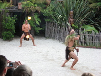Two Maori 'warriors' in an arena, one waving a staff and the other a flaming stick.