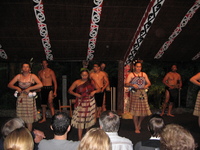 Maori in traditional dress singing and dancing on stage in front of a crowd.
