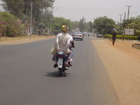 Eleanor clinging to the back of a motorbike, on a quiet road in Kaduna
