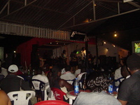 A small stage with a crowd of people sitting at plastic tables in front of it