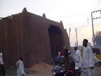 A mud-built gate, with traffic in front of it