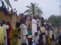 Brightly-dressed people watching the Durbar, some sitting on the wall