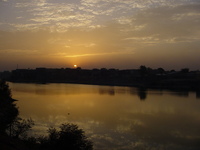 The sun sets over a small lake, with Kano's old city in the background