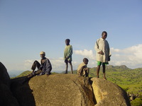 An old man and a few boys (including one in green shorts) on top of a rock