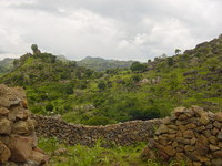 Huts, trees, crops and rocks in a hilly landscape
