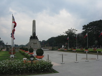 A tall monument in a park, surrounded by Philippines flags.