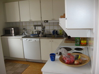 A kitchen, metal worksurfaces and white cabinets.  Pots and coffee-making equipment are scattered around.