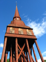 A red wooden belfry with shingled legs against a blue sky.