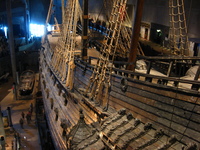 A wooden sailing ship in a museum buidling, people milling around down by the keel.