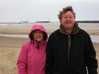 Mum and Dad standing on a sandy beach.  In the background are artificial rock reefs and the lagoons they have created.