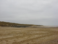 A sandy beach under grey skies.  Grassy dunes are on the left, stretching into the distance.