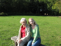 Granny and Eleanor sitting on a wooden bench on a lawn.