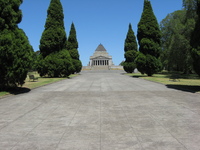 A wide avenue leads up to a striking building, something like a Greek temple with a pyramid on top.  Behind it is a clear blue sky.