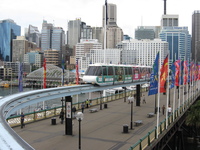 The Sydney monorail crossing Pyrmont Bridge at Darling Harbour. In front of skyscrapers a monorail train approaches a station.