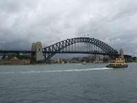 A coathanger-like steel bridge crosses a harbour.  A ferry is to the right of the foreground.