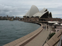 A building made of what look like large, white concrete shells sits beside a harbour.