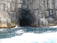 A small cave in a cliff face, the sea foaming in and around the cave.