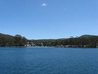 A group of stone buildings set in what appears to be parkland are seen from a bay.