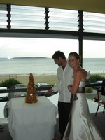 Lee wraps one arm around Hannah while he cuts the wedding cake (a pyramid of profiteroles) with the other.