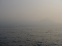 A conical mountain is just visible through mist across the sea
