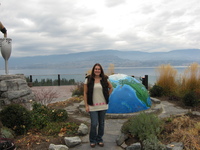 Tammie outside the Summerhill Pyramid winery Tammie standing in front of a large globe, half-sunk into the ground. Behind her is a lake and mountains.