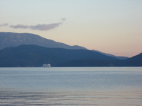 Sea and mountains, in the distance a white ferry is coming towards the camera.