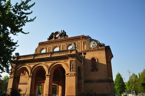 Part of the ruined façade of a building, in orange-yellow stone, against a clear blue sky with a park behind it.