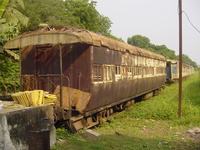 A rusty and collapsing railway carriage with wooden shutters on the windows and an open-platform at each end.