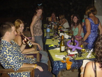 People sitting around a table in the dark.  The table is covered in the debris of a meal, empty bottles and crackers.