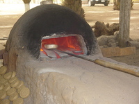 A clay furnace with a ceramic mold being put in on a long tool.