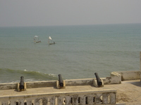 Cannons pointing out to sea from castle battlements towards fishing boats with patchwork sails.