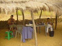 Dave and Marebec reading by a plastic table under a thatched roof.