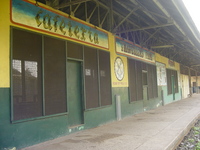 Railway station platform building painted green and yellow, over the doors and windows are two signs 'Cafeteria' and 'Travellers Fare'.  Between two windows is a painted logo and 'Railway Catering Service'.