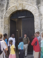 A wooden gate in a stone arch, signed 'Door of Return'.  People standing in the gateway.