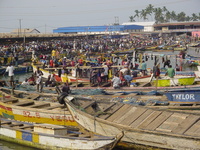 A chaotic jumble of brightly-painted fishing boats and people in front of open-sided sheds.