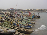 Colourful fishing boats (large canoes) adorned with flags packed into a small harbour.