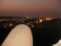 A rusty cannon points out towards a lagoon and streetlights at sunset.