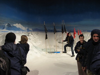 People dressed in warm jackets standing around in a room which a snow floor and painted views of Antarctica on the walls.