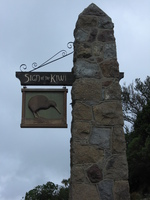 A painted wooden sign showing a kiwi hangs from a stone post.