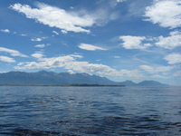 View across the sea to a headland with mountains in the distance.