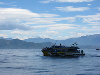 A blue and yellow catamaran on the sea in front of mountains.